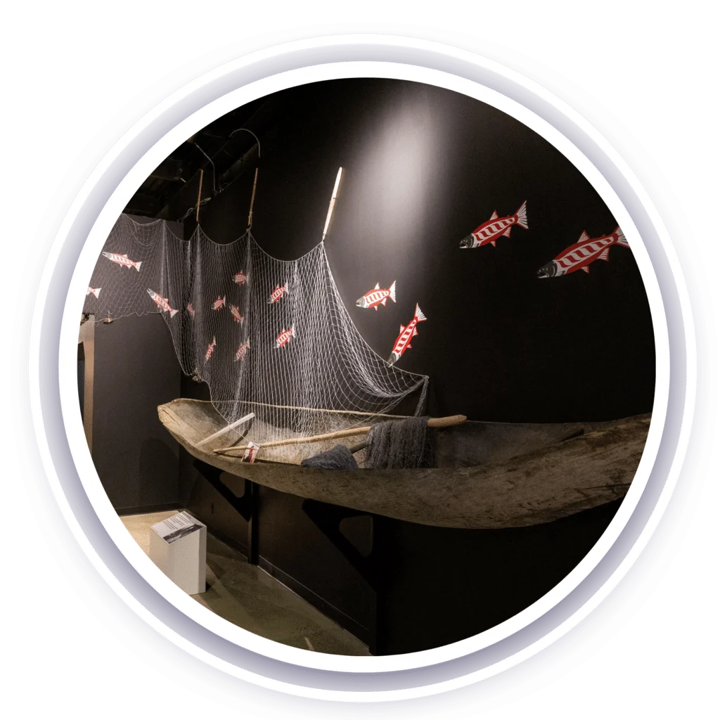 A dugout canoe hangs on the wall, draped with a fishing net. Red, white, and green stickers depicting fish are arranged on the wall